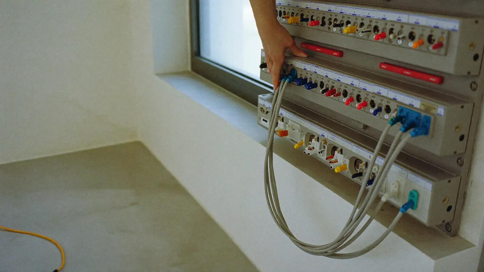 Close-up of a hand testing a warm circuit breaker at a home panel next to a wall-mounted EV charger