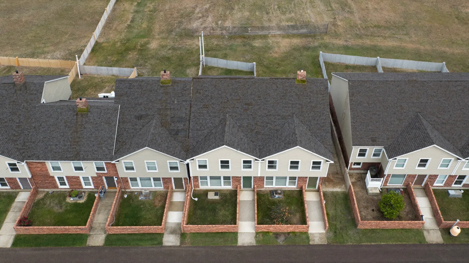 Aerial view of a row of attached US townhouses sharing continuous rooflines and brick party walls, with small walled front yards