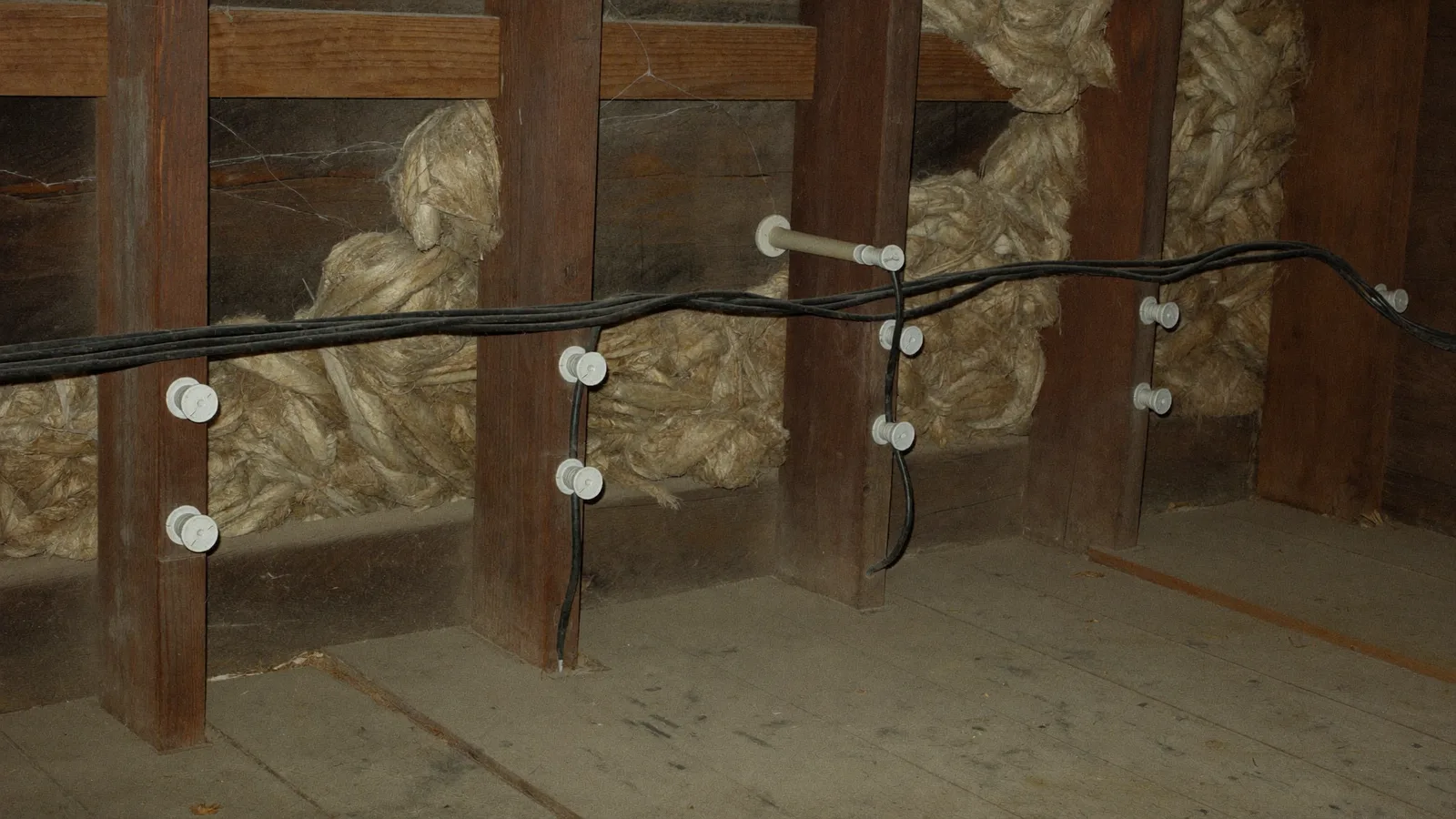 Knob-and-tube wiring in an attic: porcelain knobs on joists carrying separate cloth-covered conductors